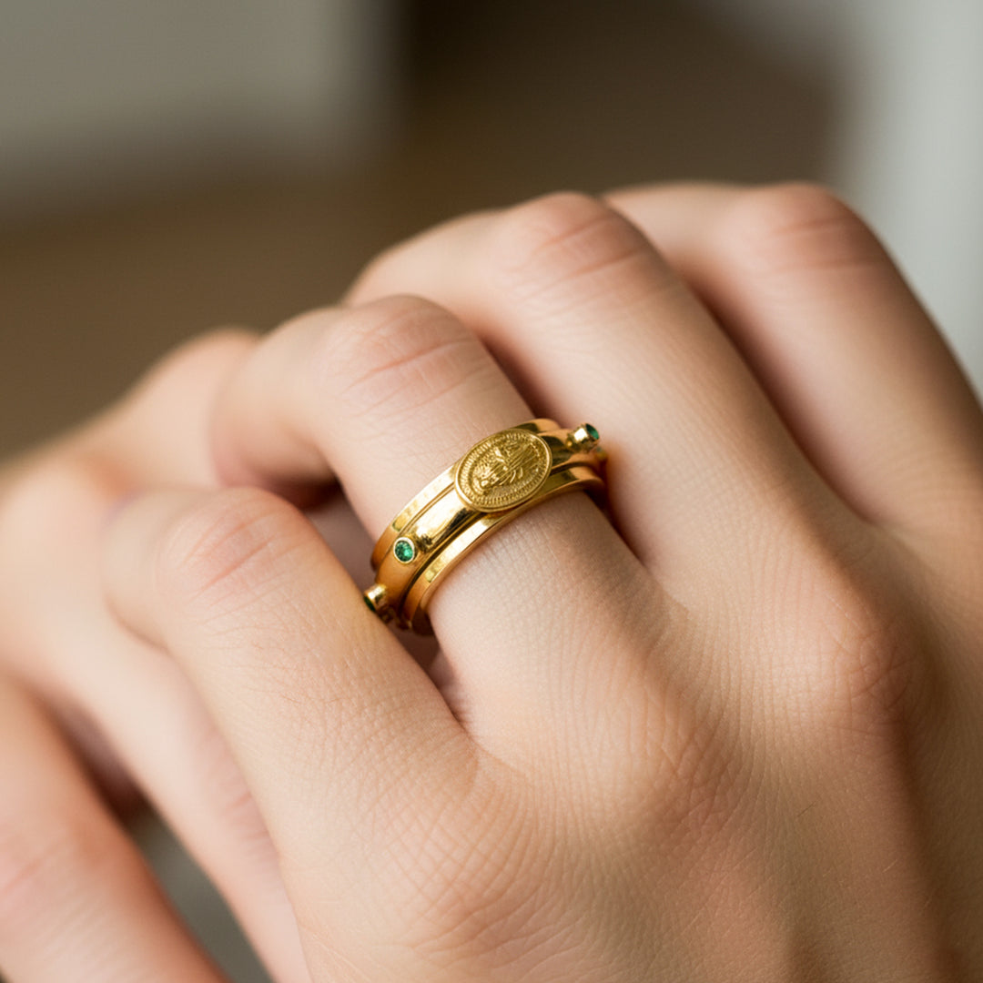 Mano de mujer usando un anillo denario con movimiento en oro amarillo de 18 quilates con Esmeraldas naturales de Joyería Caracas. 