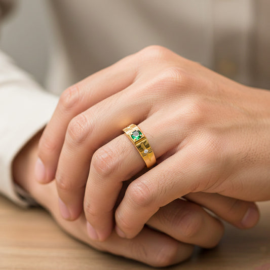 Mano de hombre usando un anillo en oro amarillo de 18 quilates con formas de destellos, un cristal verde en el centro y dos blancos en los laterales de Joyería Caracas. 