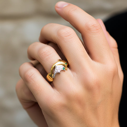 Mano de mujer usando un anillo con la forma de un delfín mamá e hijo en oro amarillo y blanco de 18 quilates con cristales de Joyería Caracas. 
