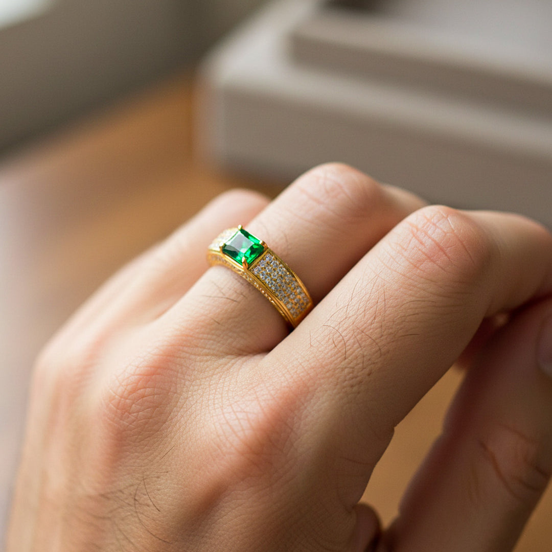 Mano de hombre usando un anillo en oro amarillo de 18 quilates con Esmeralda en corte baguette y cristales blancos de Joyería Caracas. 