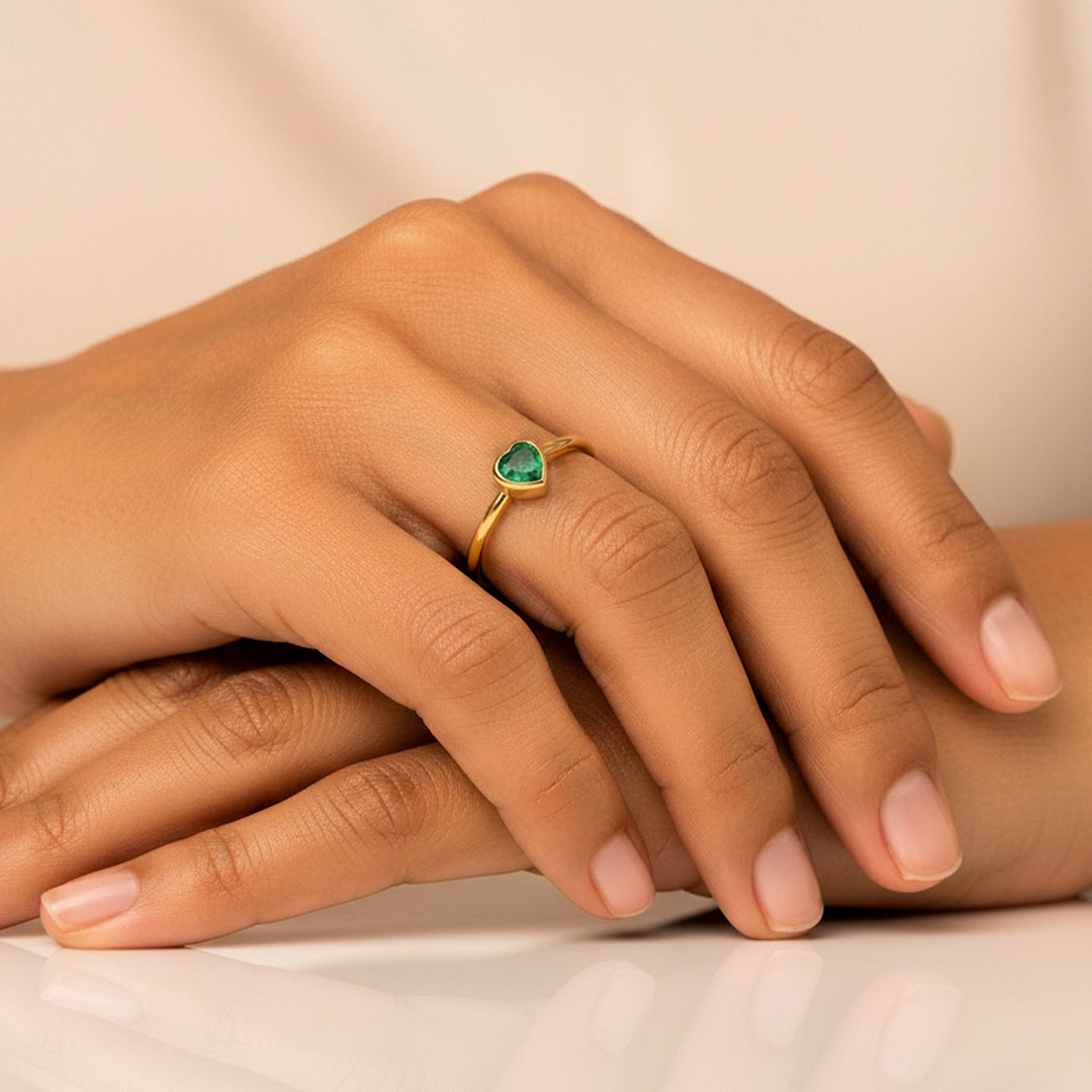 Mano de mujer usando un anillo en oro amarillo de 18 quilates con Esmeralda en forma de corazón en el centro de Joyería Caracas. 