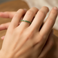Mano de mujer usando un anillo sin fin en oro amarillo de 18 quilates con cristales de color verde alrededor de Joyería Caracas. 