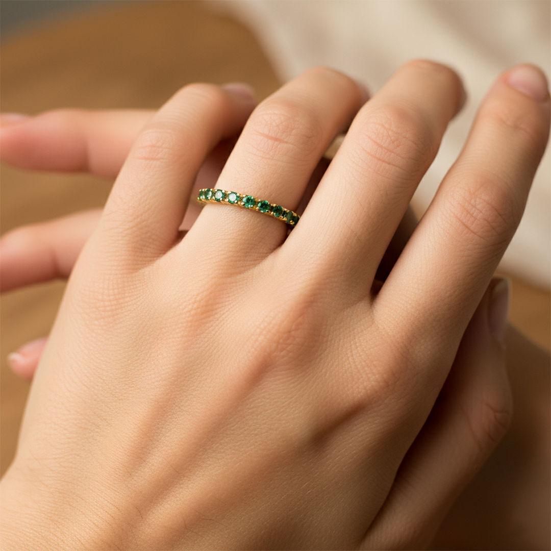 Mano de mujer usando un anillo sin fin en oro amarillo de 18 quilates con cristales de color verde alrededor de Joyería Caracas. 