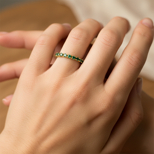 Mano de mujer usando un anillo sin fin en oro amarillo de 18 quilates con cristales de color verde alrededor de Joyería Caracas. 