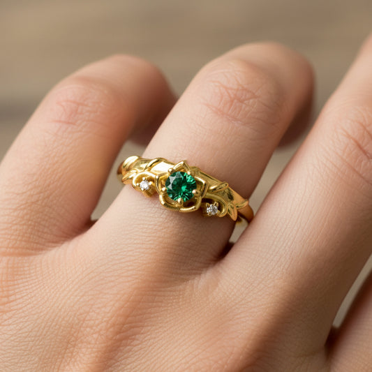 Mano de mujer usando un anillo de espinas y rosas en oro amarillo de 18 quilates con cristales de color blanco y 1 cristal de color verde en el centro de Joyería Caracas. 