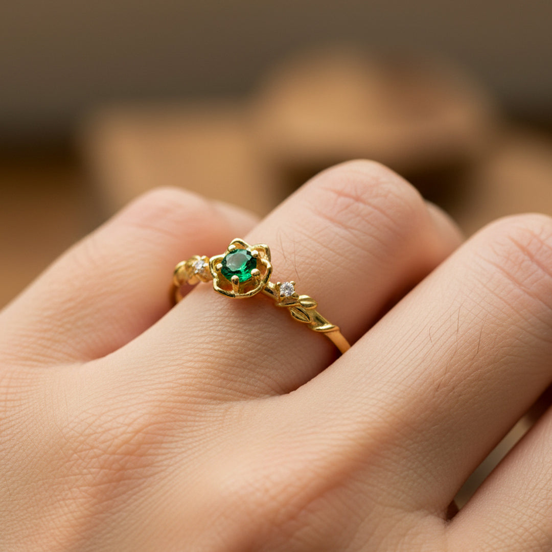 Mano de mujer usando un anillo de espinas y rosas en oro amarillo de 18 quilates con cristales de color blanco y cristal de color verde en el centro de Joyería Caracas. 