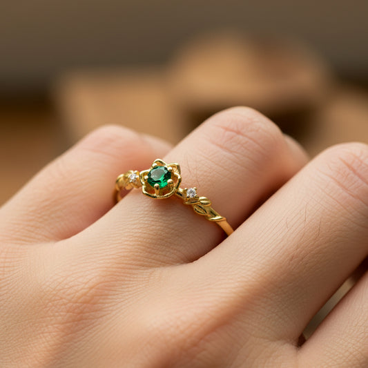 Mano de mujer usando un anillo de espinas y rosas en oro amarillo de 18 quilates con cristales de color blanco y cristal de color verde en el centro de Joyería Caracas. 