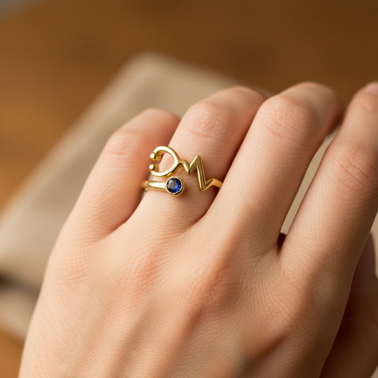 Mano de mujer usando un anillo con forma de estetoscopio en oro amarillo de 18 quilates con cristal de color azul de Joyería Caracas. 