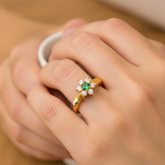 Mano de mujer usando un anillo con la forma de flor en el centro en oro amarillo de 18 quilates con cristales de color blanco y verde de Joyería Caracas. 