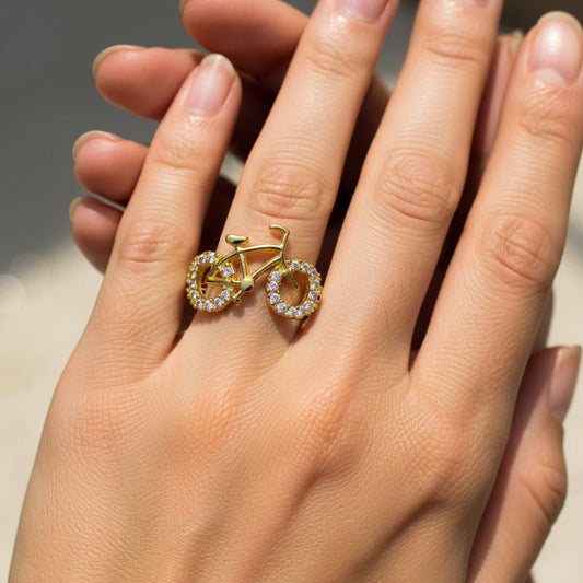 Mano de mujer usando anillo con forma de bicicleta en el centro en oro amarillo de 18 quilates con cristales de color blanco de Joyería Caracas. 