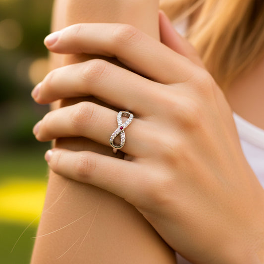 Mano de mujer usando un anillo con forma de infinito en el centro en oro blanco de 18 quilates con cristales de color blanco y rojo de Joyería Caracas. 