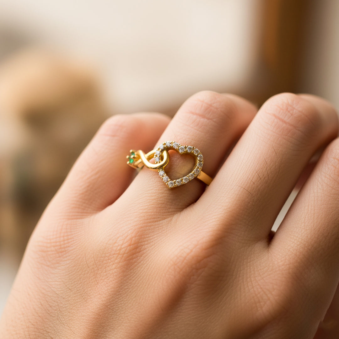Mano de mujer usando un anillo con la forma de un corazón e infinito en oro amarillo de 18 quilates y cristal de color verde de Joyería Caracas. 