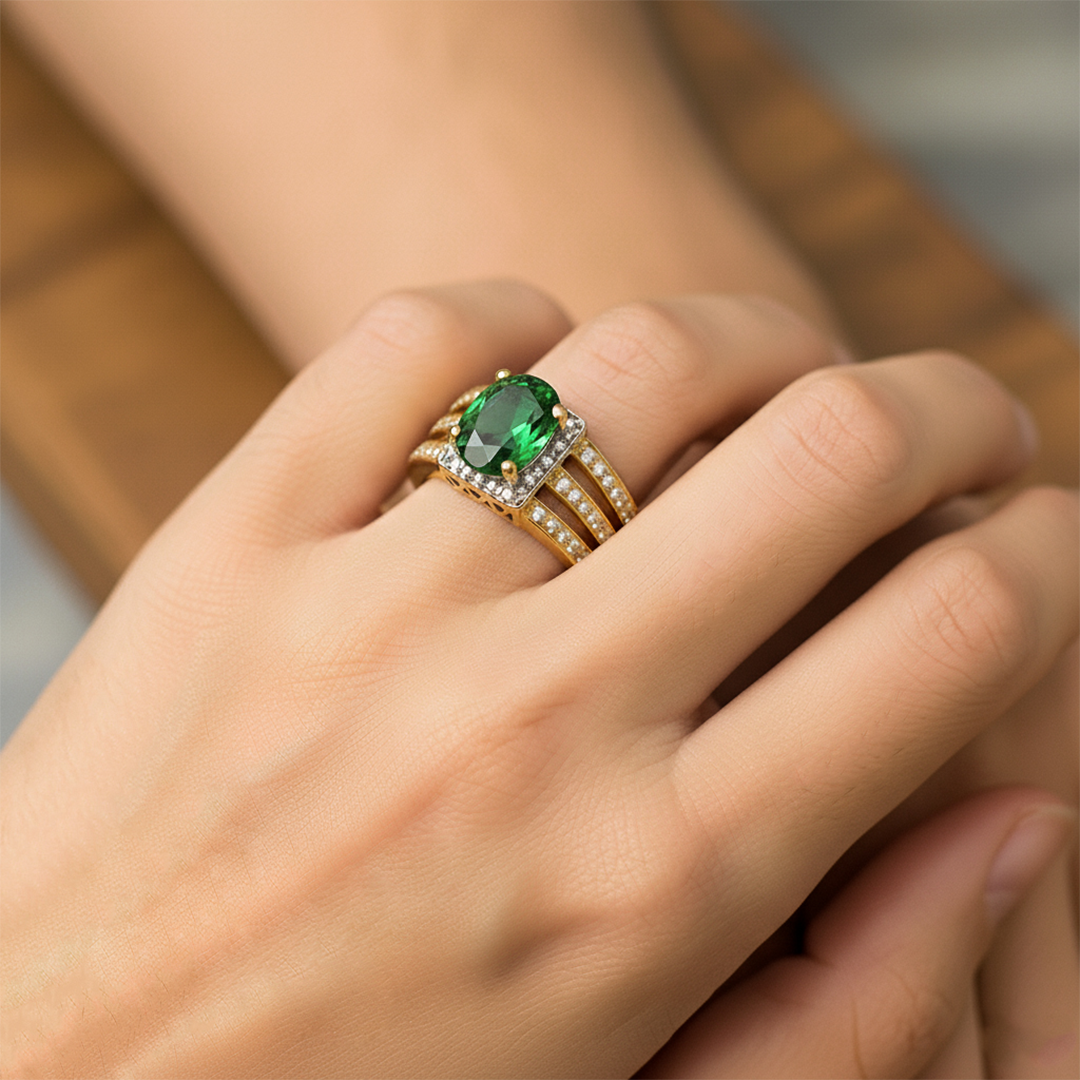 Mano de mujer usando un anillo en oro amarillo y blanco de 18 quilates con piedra ovalado sintética de color verde y Diamantes blanco alrededor de Joyería Caracas. 