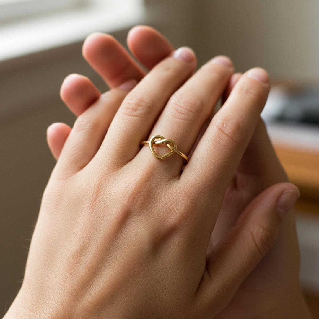Mano de mujer usando un anillo con forma de nudo de corazón en oro amarillo de 18 quilates de Joyería Caracas. 