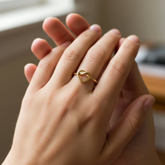 Mano de mujer usando un anillo con forma de nudo de corazón en oro amarillo de 18 quilates de Joyería Caracas. 