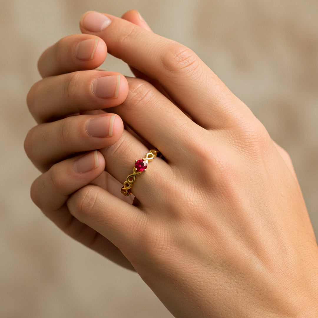 Mano de modelo usando un anillo de infinitos en oro amarillo de 18 quilates con cristal de color rojo de Joyería Caracas. 