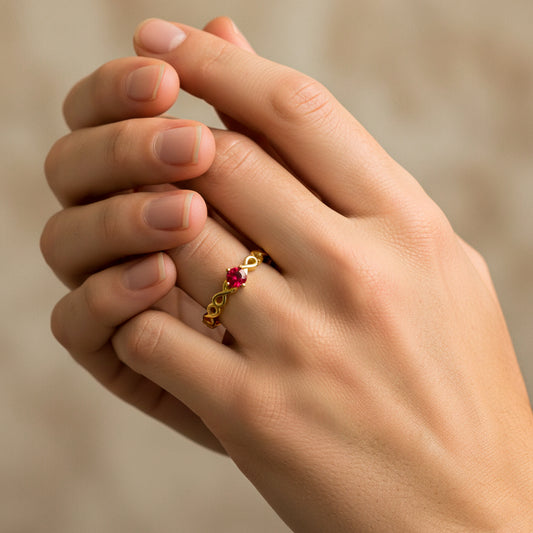 Mano de modelo usando un anillo de infinitos en oro amarillo de 18 quilates con cristal de color rojo de Joyería Caracas. 