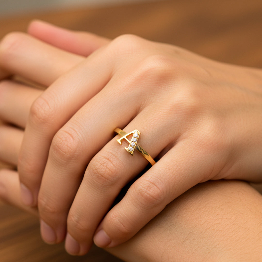 Mano de mujer usando un anillo con la Letra A en el centro en oro amarillo de 18 quilates con cristales de color blanco de Joyería Caracas. 