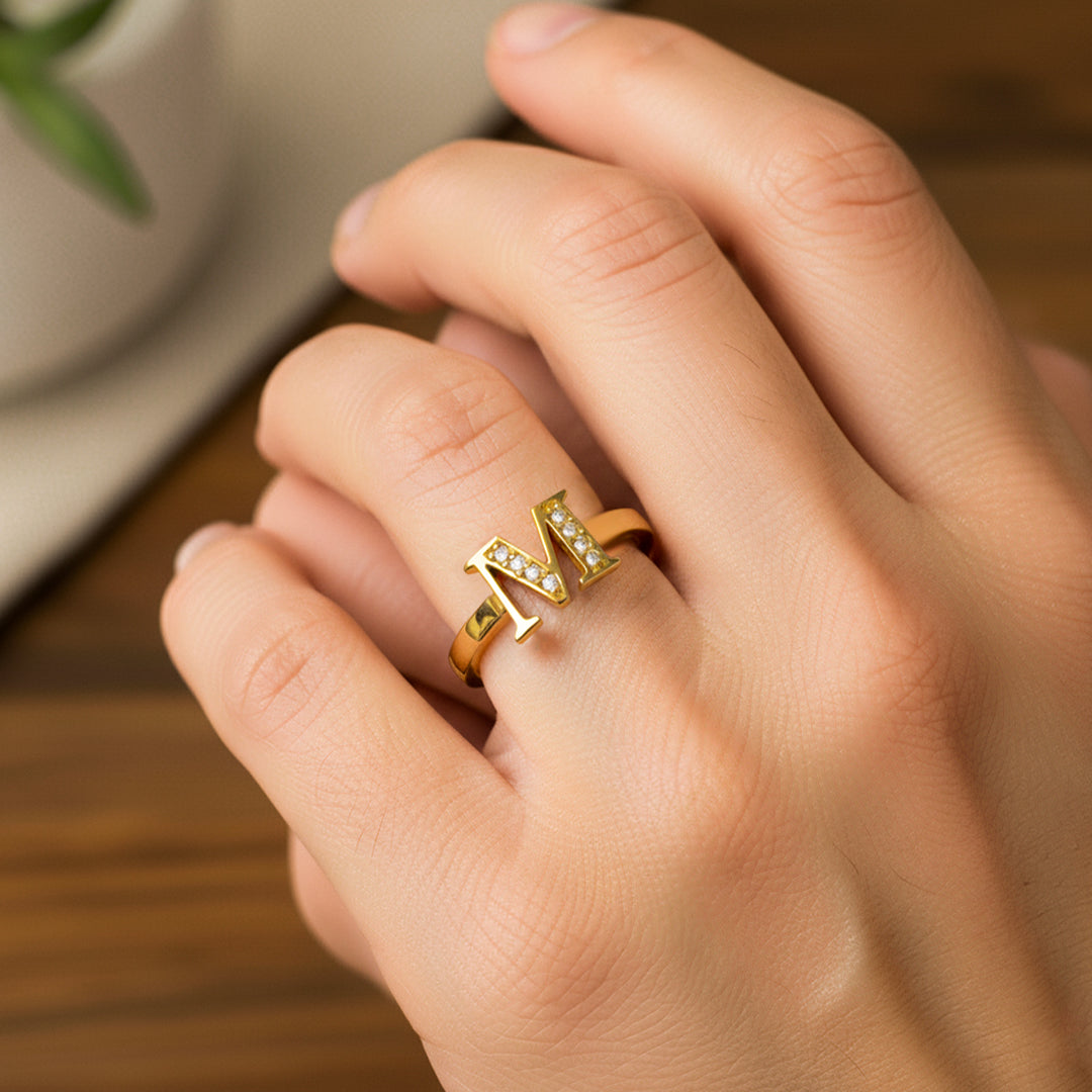 Mano de mujer usando un anillo con la letra M en oro amarillo de 18 quilates de Joyería Caracas. 