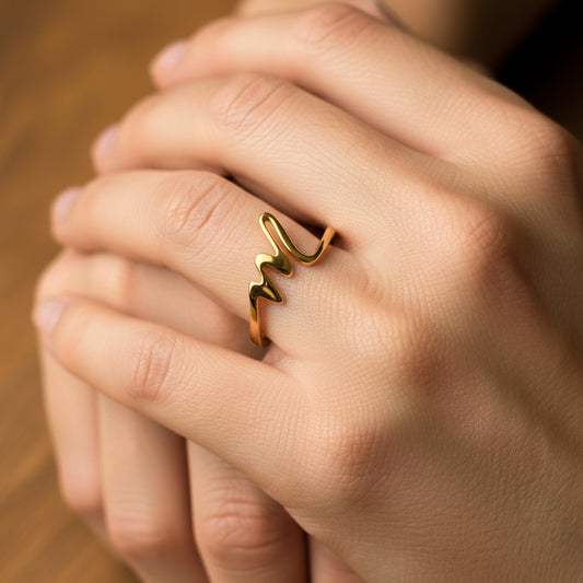 Mano de mujer usando un anillo de letra M en cursiva mini en oro amarillo de 18 quilates de Joyería Caracas. 