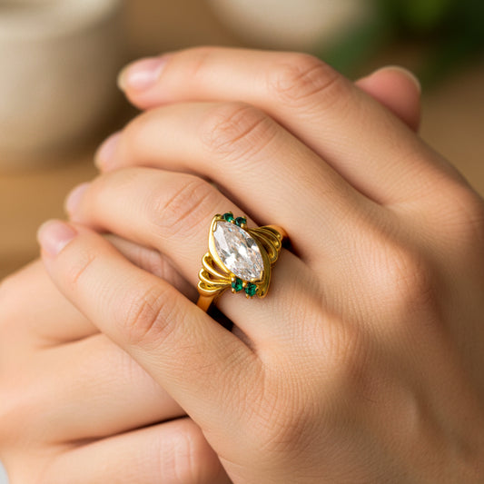 Mano de mujer usando un anillo en oro amarillo de 18 quilates con piedra central en forma Marquise con Esmeraldas de Joyería Caracas. 