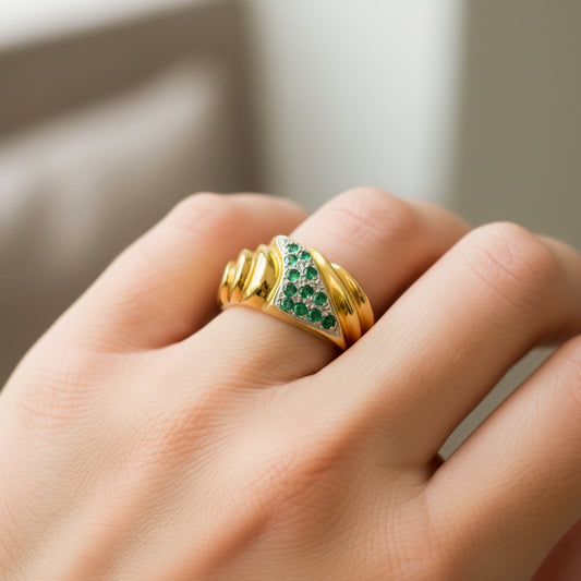 Mano de mujer usando un anillo en oro amarillo y blanco con forma de ola y Esmeraldas de Joyería Caracas. 