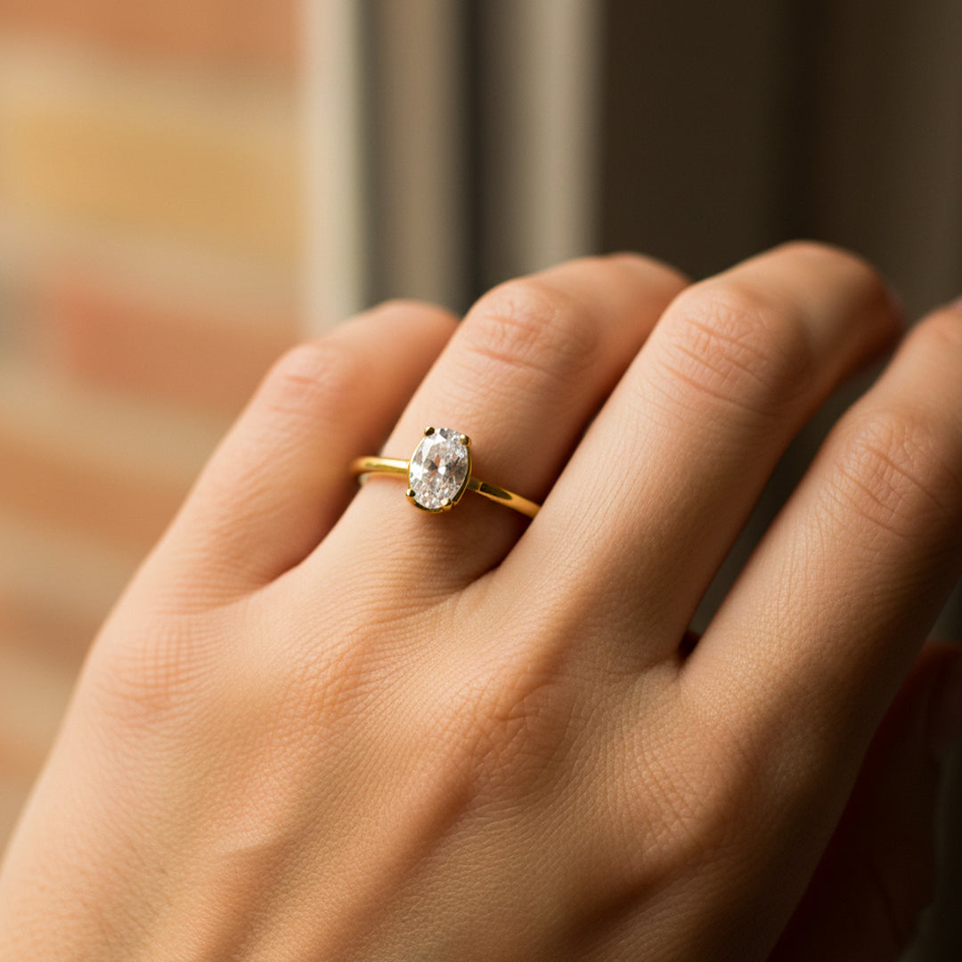 Mano de mujer usando un anillo en oro amarillo de 18 quilates con cristal ovalado de color blanco de Joyería Caracas. 