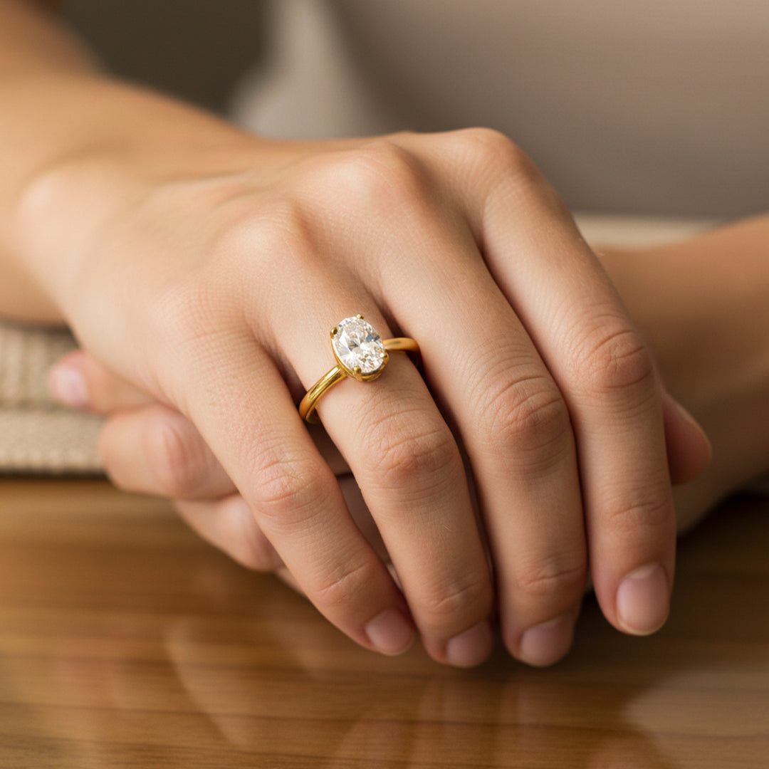 Mano de mujer usando un anillo en oro amarillo de 18 quilates con cristal ovalado de color blanco de Joyería Caracas. 