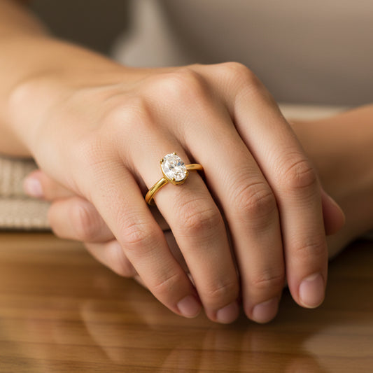 Mano de mujer usando un anillo en oro amarillo de 18 quilates con cristal ovalado de color blanco de Joyería Caracas. 