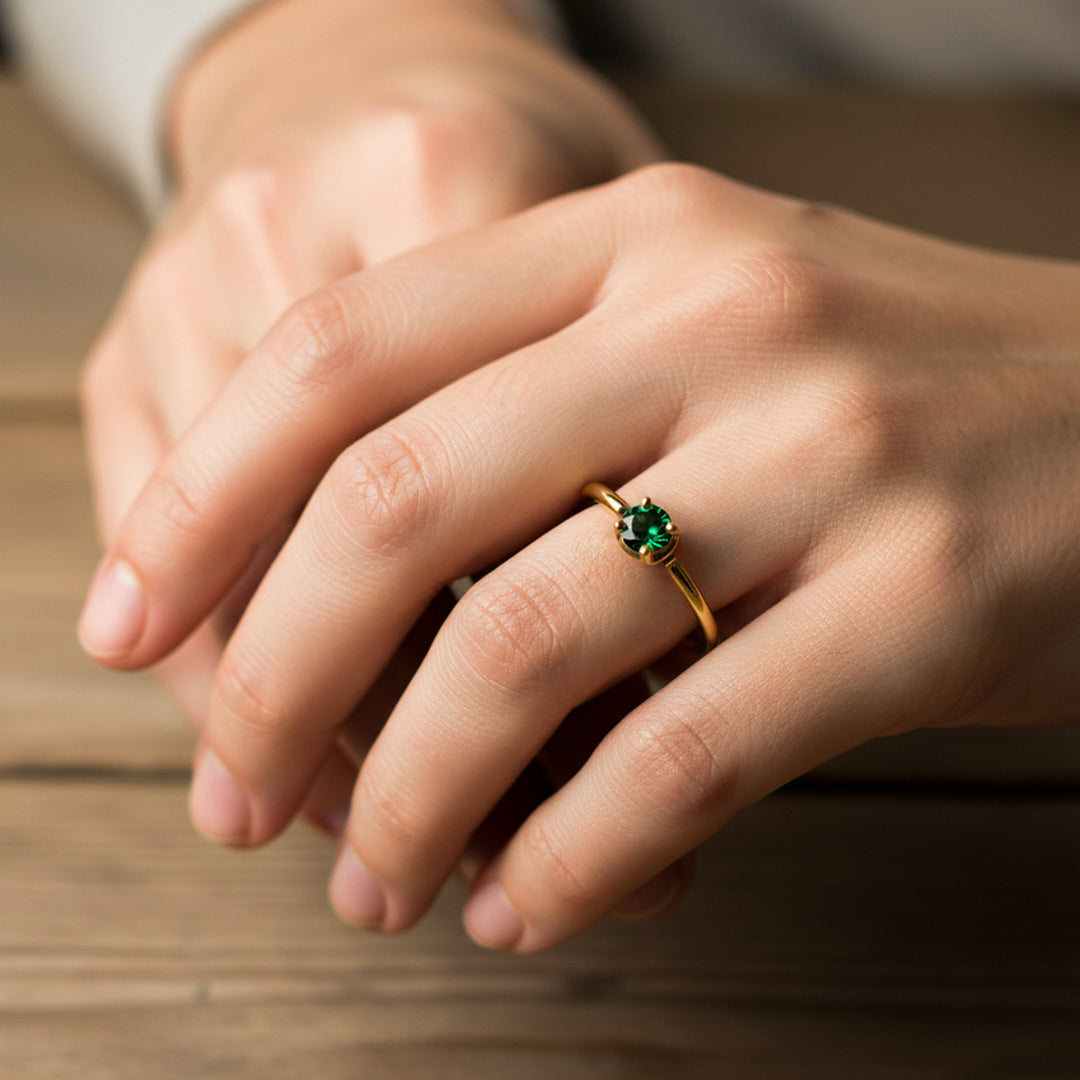 Mano de mujer usando un anillo en oro amarillo de 18 quilates con cristal redondo de color verde de Joyería Caracas. 