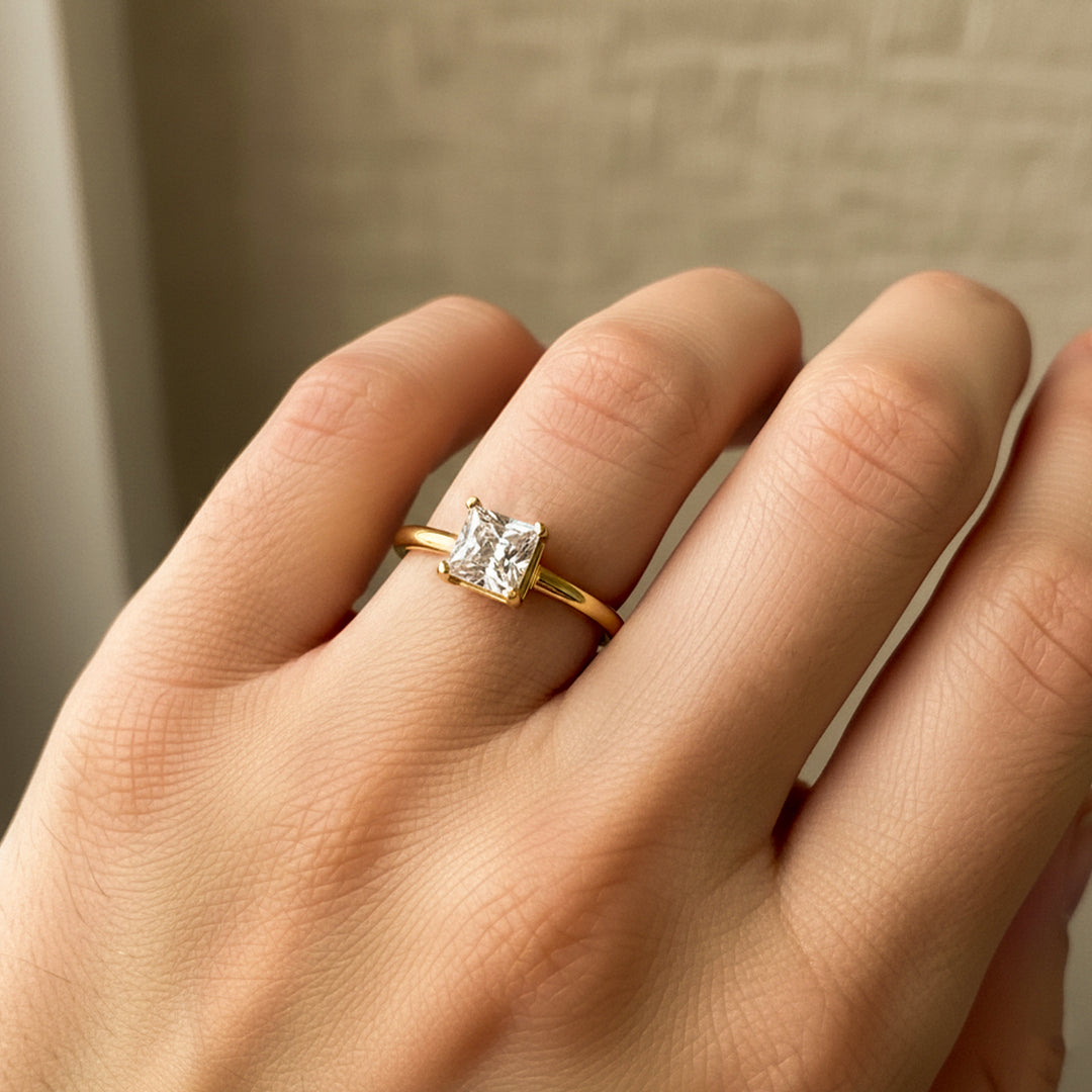 Mano de mujer usando un anillo en oro amarillo de 18 quilates con cristal cuadrado en el centro de color blanco de Joyería Caracas. 