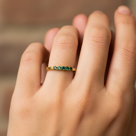 Mano de mujer usando un anillo en oro amarillo de 18 quilates con 5 cristales de color verde en el centro de Joyería Caracas. 