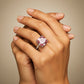 Mano de modelo usando un anillo en oro blanco de 18 quilates con Zafiro (sintético) en tonalidades rosas y anaranjadas ubicado en el centro acompañado de Moissanitas de color blanco alrededor fabricado en Joyería Caracas. 