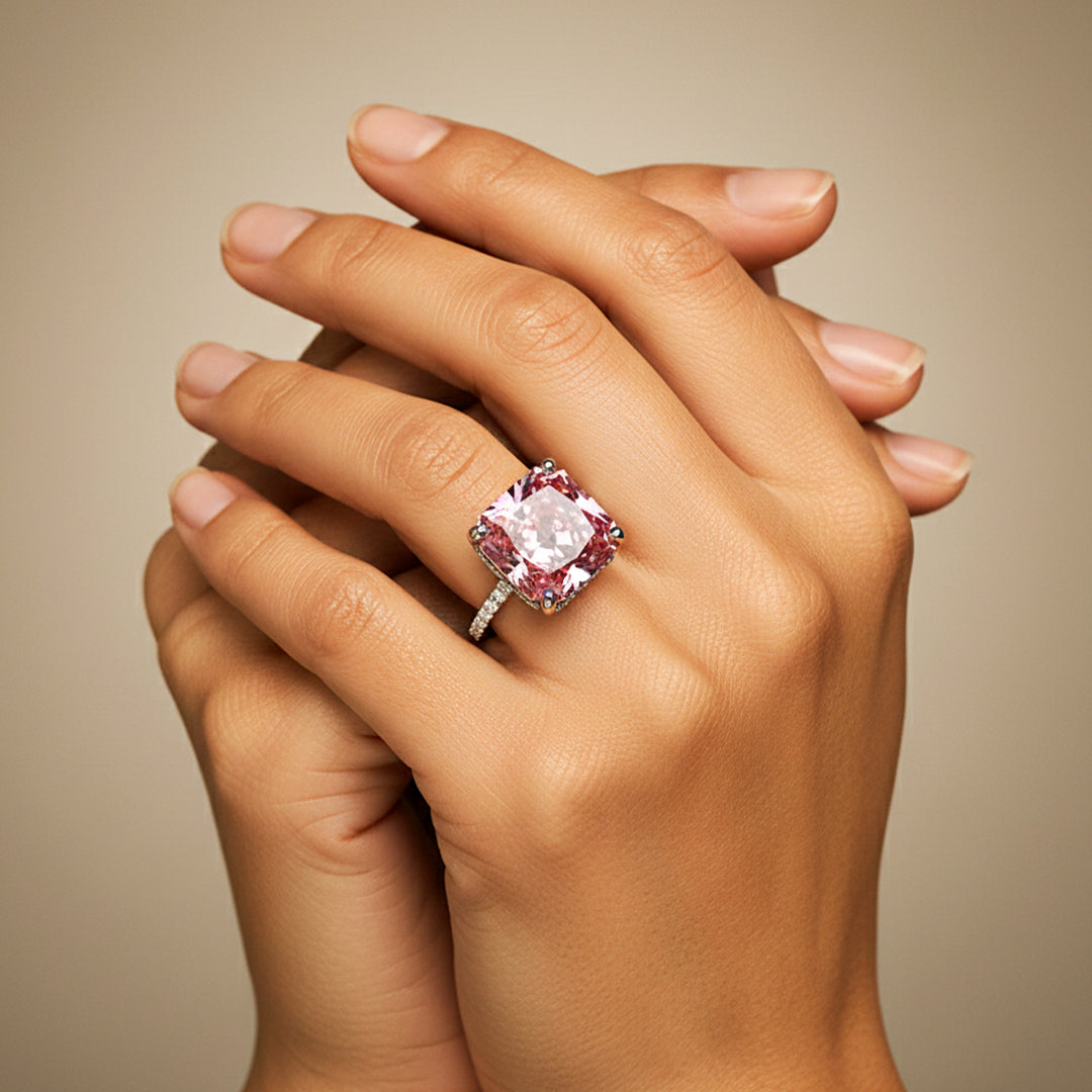 Mano de modelo usando un anillo en oro blanco de 18 quilates con Zafiro (sintético) en tonalidades rosas y anaranjadas ubicado en el centro acompañado de Moissanitas de color blanco alrededor fabricado en Joyería Caracas. 