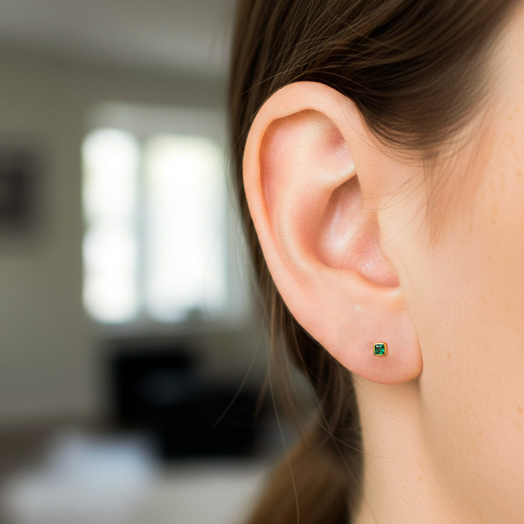 Oreja de modelo usando un topito en oro amarillo de 18 quilates con Esmeralda en corte de princess de Joyería Caracas. 