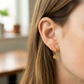 Oreja de modelo usando unos aretes sin fin con dije de San Benito en oro amarillo de 18 quilates de Joyería Caracas. 