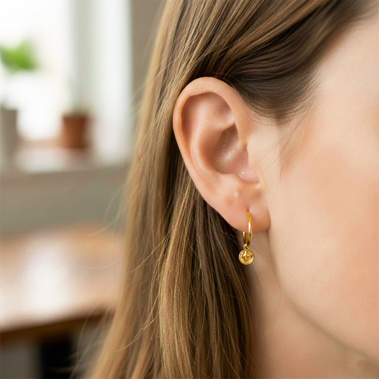 Oreja de modelo usando unos aretes sin fin con dije de San Benito en oro amarillo de 18 quilates de Joyería Caracas. 