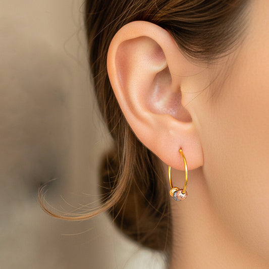 Oreja de modelo usando unos aretes sin fin en oro amarillo y 3 esferas 3 oros de 18 quilates de Joyería Caracas. 