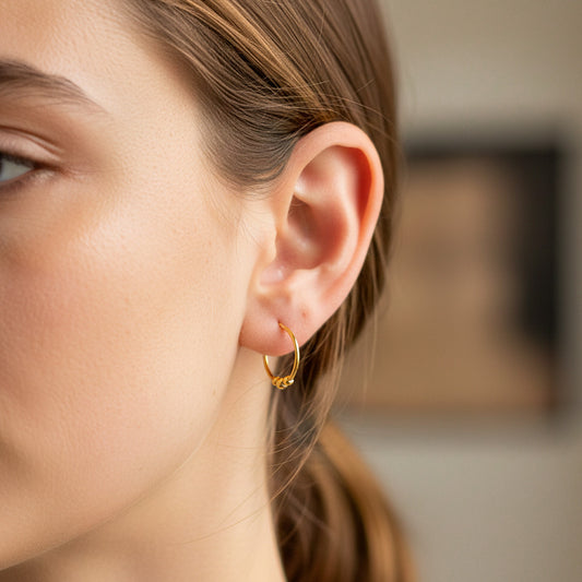 Oreja de modelo usando unos aretes sin fin con esferas en oro amarillo de 18 quilates de Joyería Caracas. 