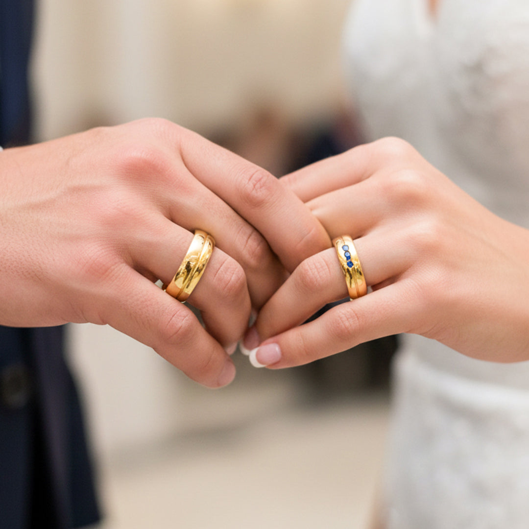 Manos de una pareja usando unas argollas de matrimonio en oro amarillo de 18 quilates con Zafiros de Joyería Caracas. 