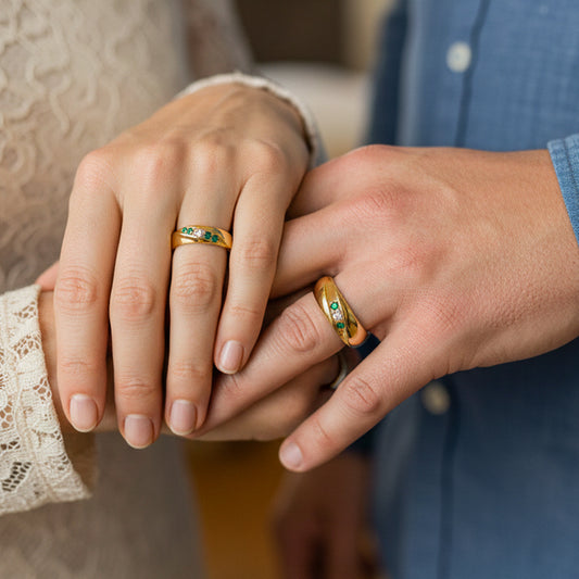 Mano de pareja en matrimonio usando unas argollas en oro amarillo de 18 quilates con Esmeraldas y Diamantes de Joyería Caracas. 