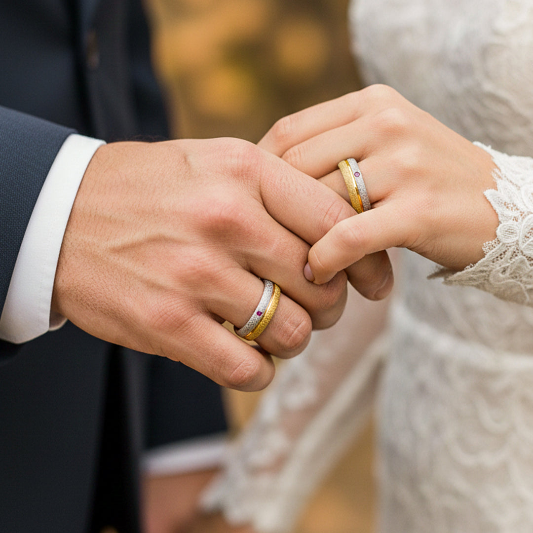Mano de pareja en matrimonio usando unas argollas en oro amarillo y blanco de 18 quilates con Rubí de Joyería Caracas. 