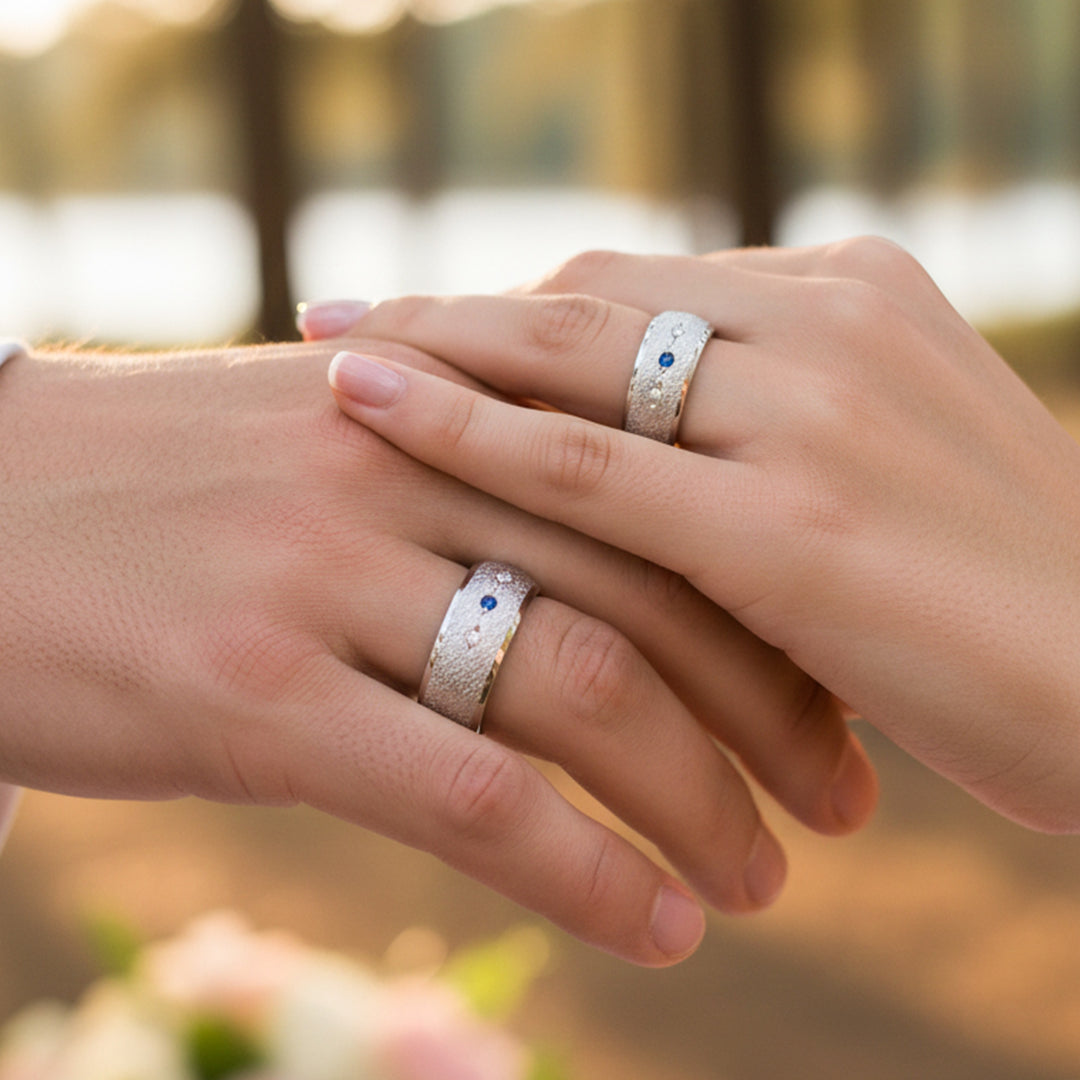 Manos de pareja usando unas argollas de matrimonio en oro blanco de 18 quilates con Zafiro y Diamantes de Joyería Caracas. 