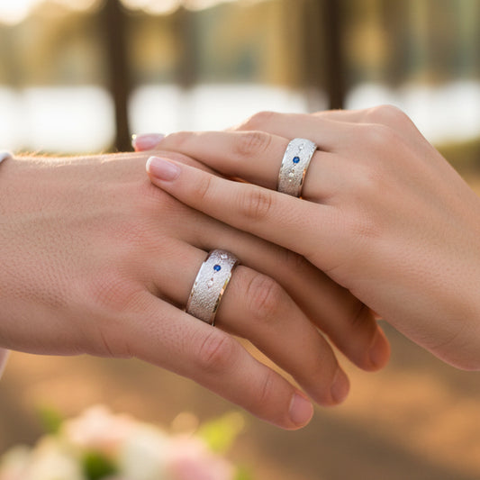 Manos de pareja usando unas argollas de matrimonio en oro blanco de 18 quilates con Zafiro y Diamantes de Joyería Caracas. 