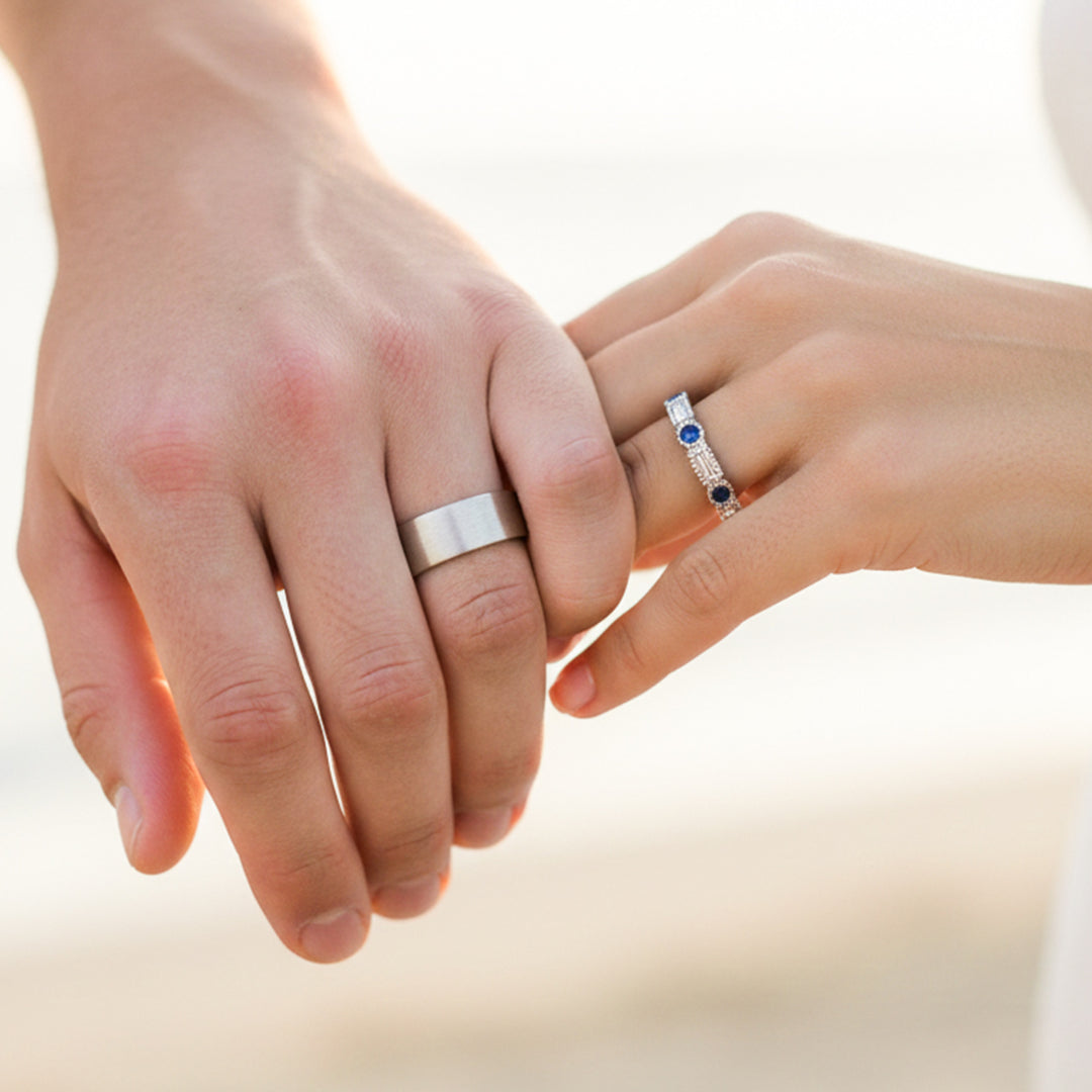 Mano de pareja usando unas argollas de matrimonio en oro blanco de 18 quilates con cristales azules y blancos de Joyería Caracas. 