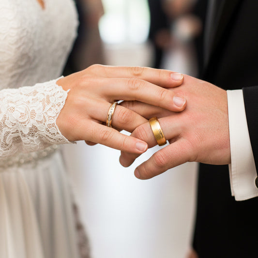 Mano de una pareja usando unas argollas de matrimonio en oro amarillo de 18 quilates con cristales para la de la dama de Joyería Caracas. 