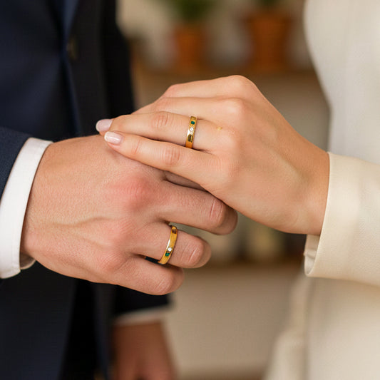 Mano de pareja en matrimonio usando unas argollas en oro amarillo de 18 quilates con Esmeraldas y Diamantes de Joyería Caracas. 