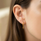 Oreja de modelo usando unas candongas lisas sin fin con dije en forma de cruz en oro amarillo de 18 quilates de Joyería Caracas. 