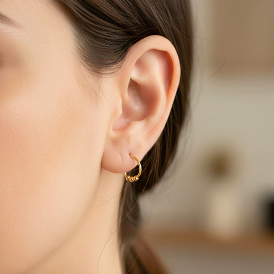 Oreja de modelo usando unas candongas sin fin con 3 esferas en oro amarillo de 18 quilates de Joyería Caracas. 