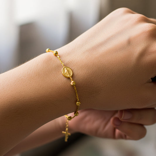 Mano de mujer usando una pulsera denario con esferas facetadas, dije de Virgen y Cruz en oro amarillo de 18 quilates de Joyería Caracas. 
